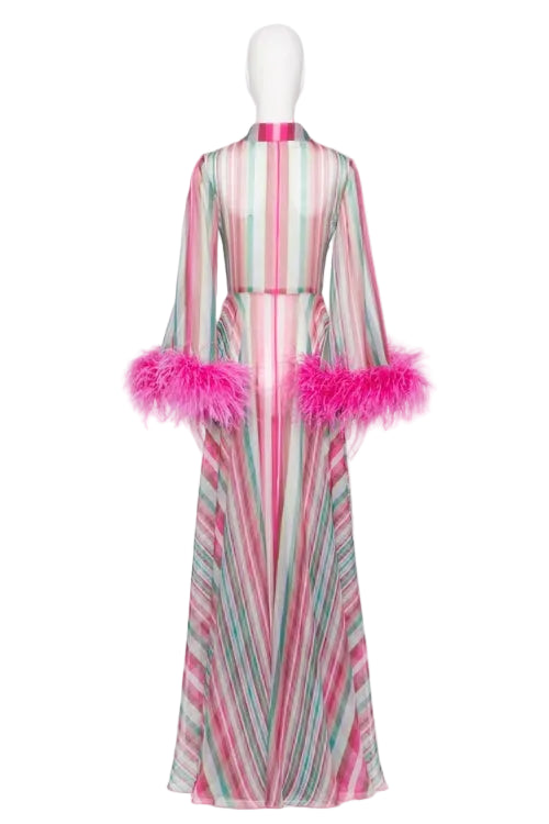 A long-sleeved maxi dress with vertical pink, green, and white stripes, featuring bright pink feather trim on the sleeves and collar, displayed on a white mannequin against a white background.