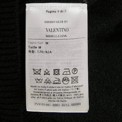 A white Valentino garment care label with size and washing instructions, photographed against a black fabric background.