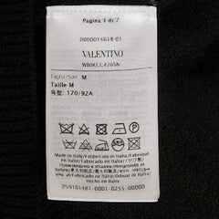A white Valentino garment care label with size and washing instructions, photographed against a black fabric background.