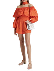 Woman wearing an orange off-shoulder top and shorts with a white handbag on a white background