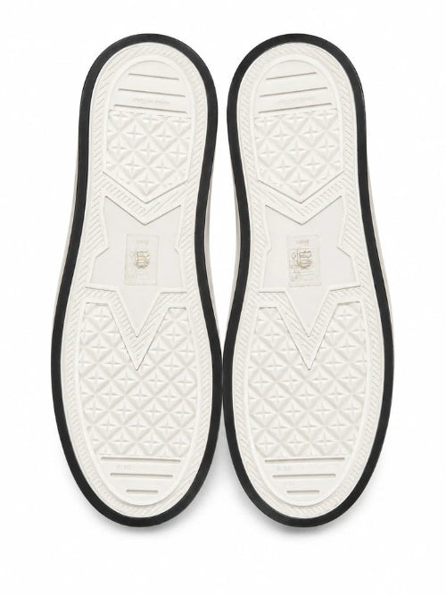 Top-down view of a pair of white slip-on shoes showing the textured outsoles with black trim, on a white background.