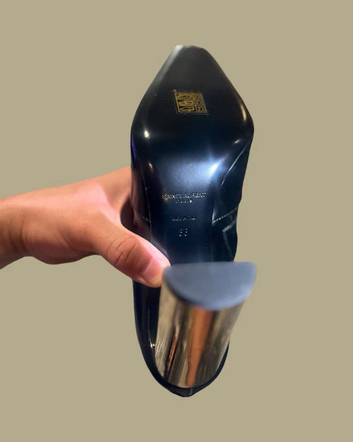 Black shoe with a blue sole held by a hand against a beige background