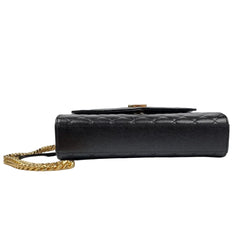 Black quilted handbag with gold chain on a light gray background