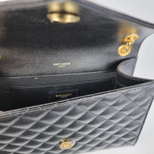 Close-up of a black quilted handbag with gold hardware, featuring the brand name.