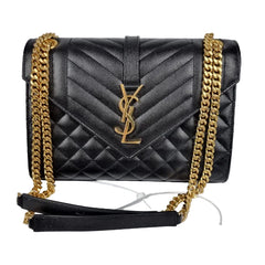 Black quilted handbag with gold chain strap on a gray background